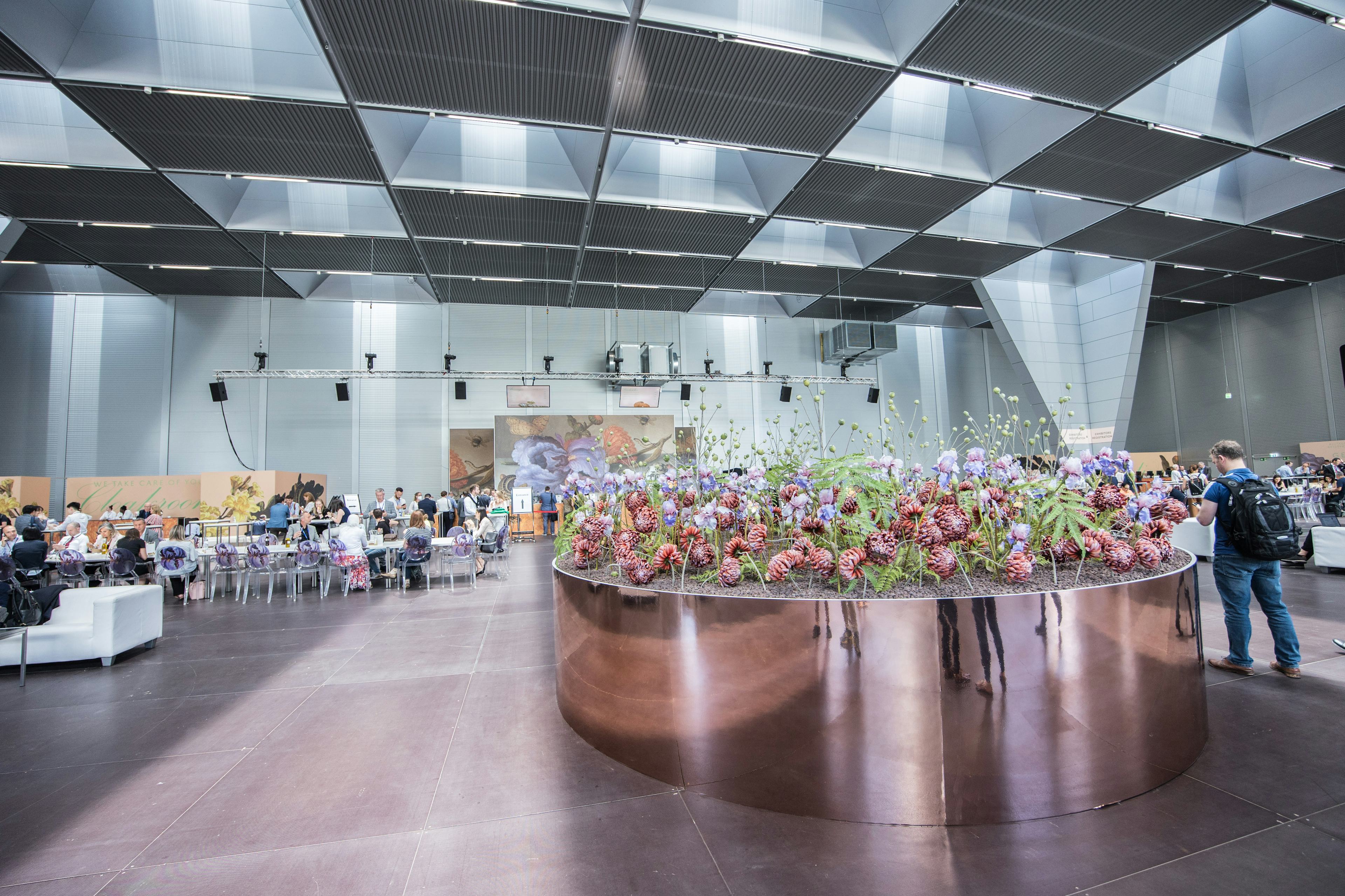 Foto: Großes Blumengesteck in einer Halle voller Menschen
