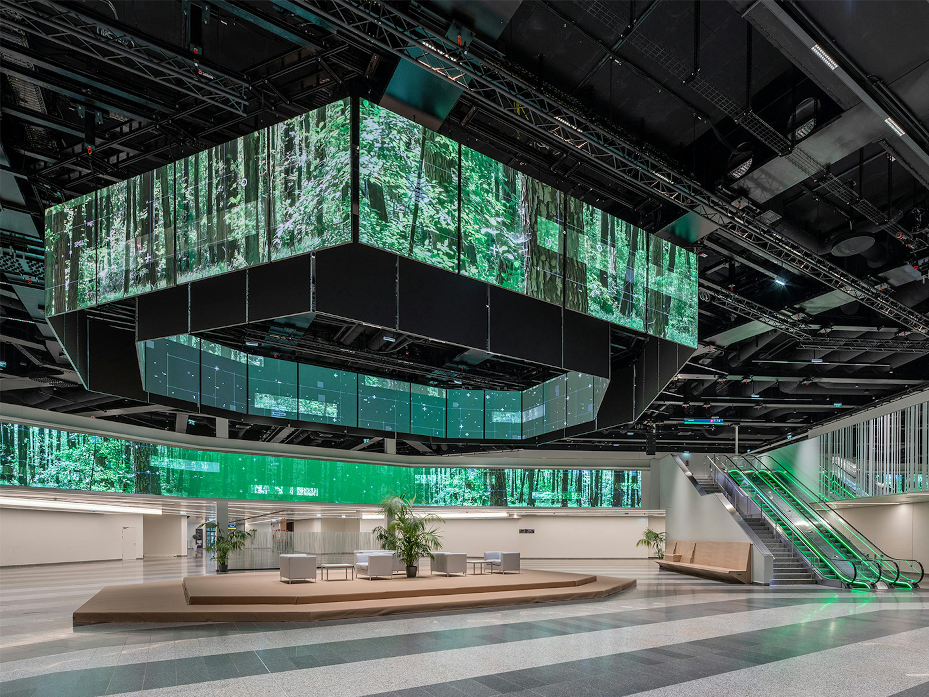 Die Eingangshalle des Austria Center Vienna mit gruen beleuchteter polySTAGE LED-Installation und Rolltreppe.