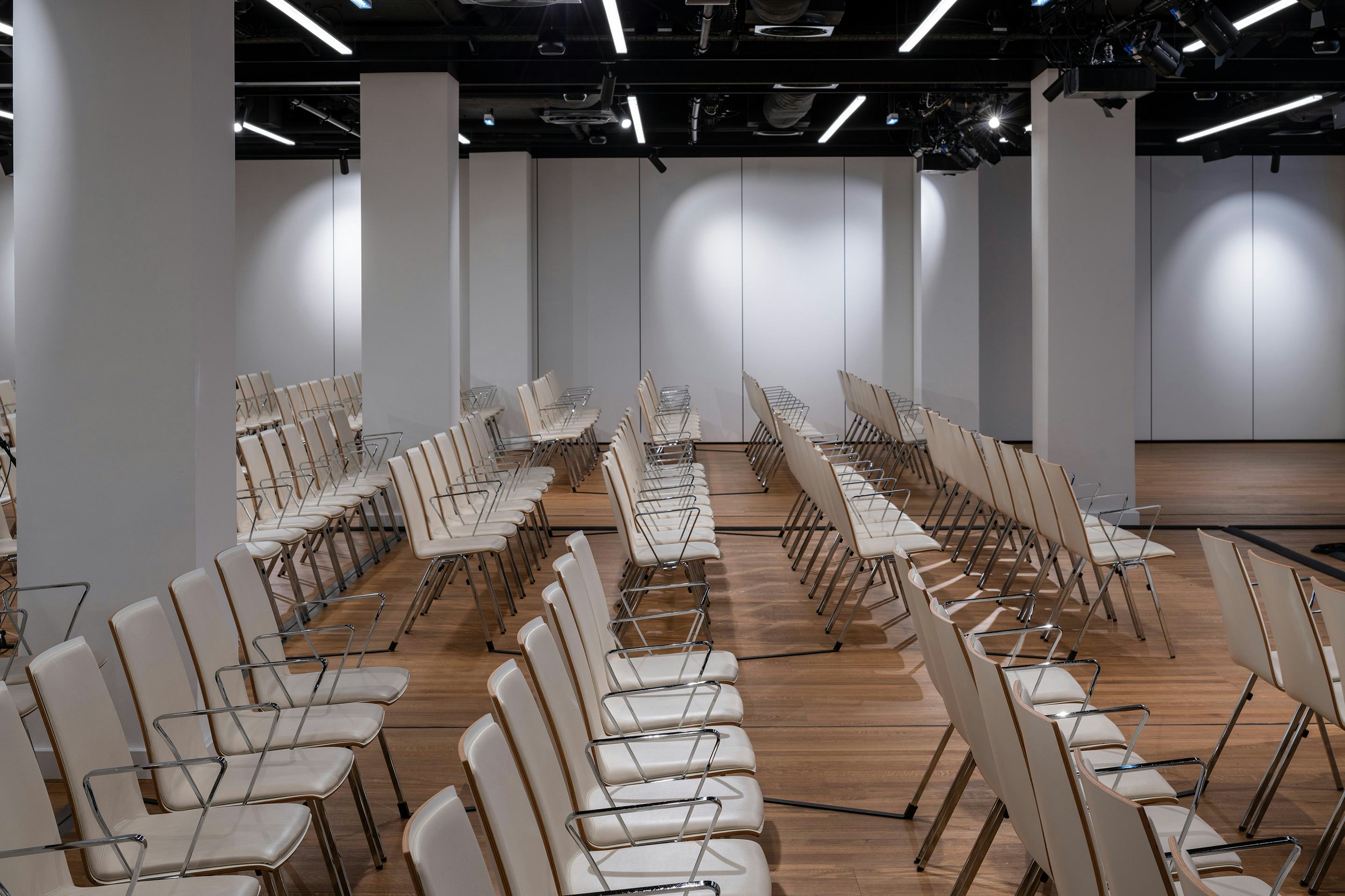 Foto: Sitzreihen in einem Saal mit Holzboden, beleuchtete Wand