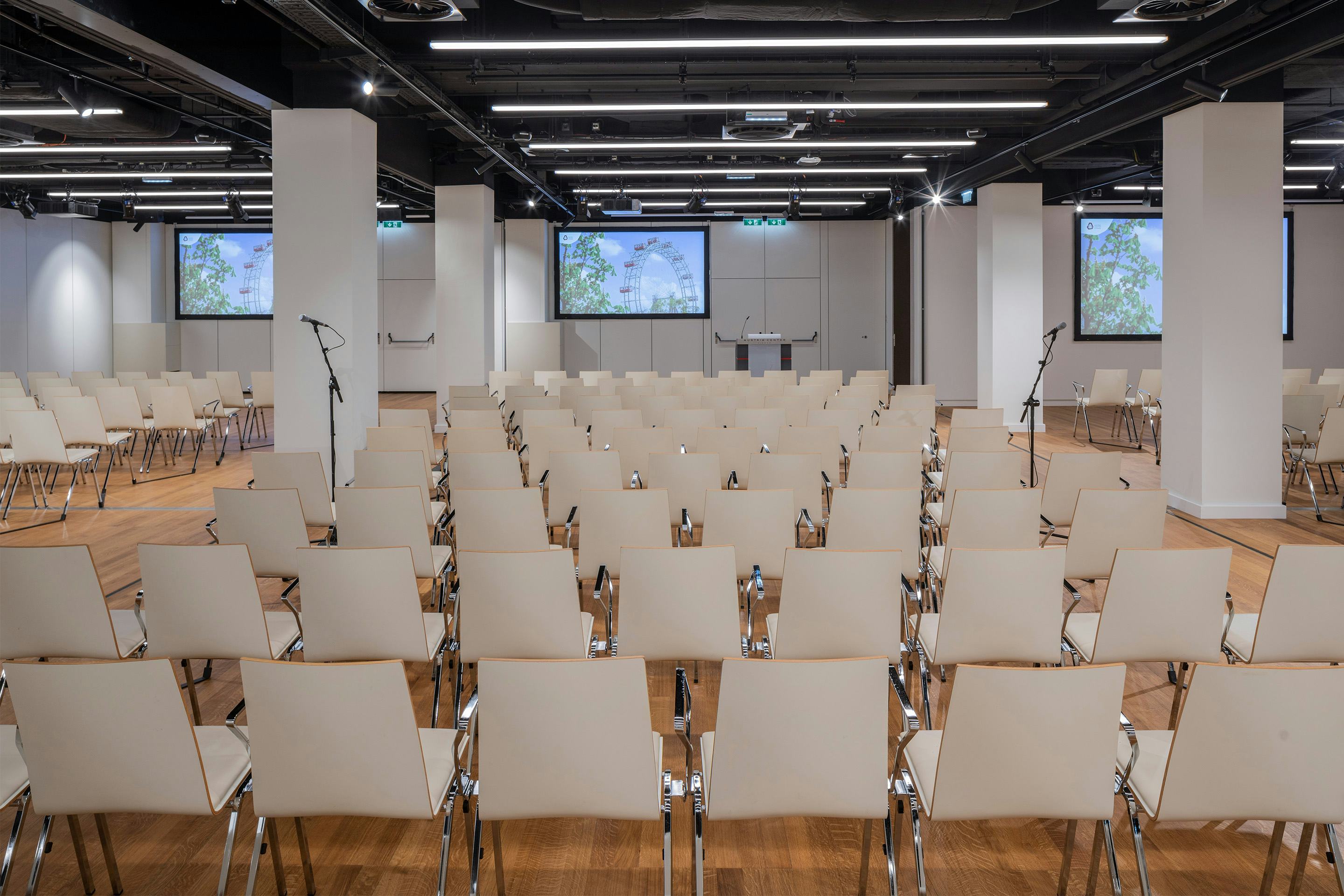 Foto: Sitzreihen in einem Saal mit Holzboden, Monitore