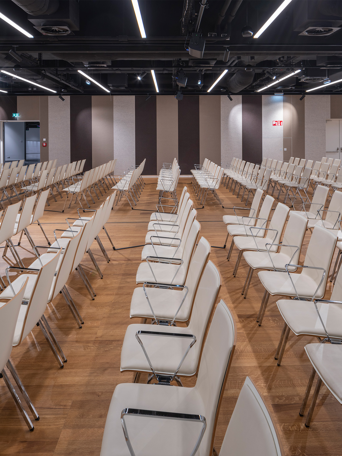Foto: Sitzreihen in einem Saal mit Holzboden, gestreifte Tapete