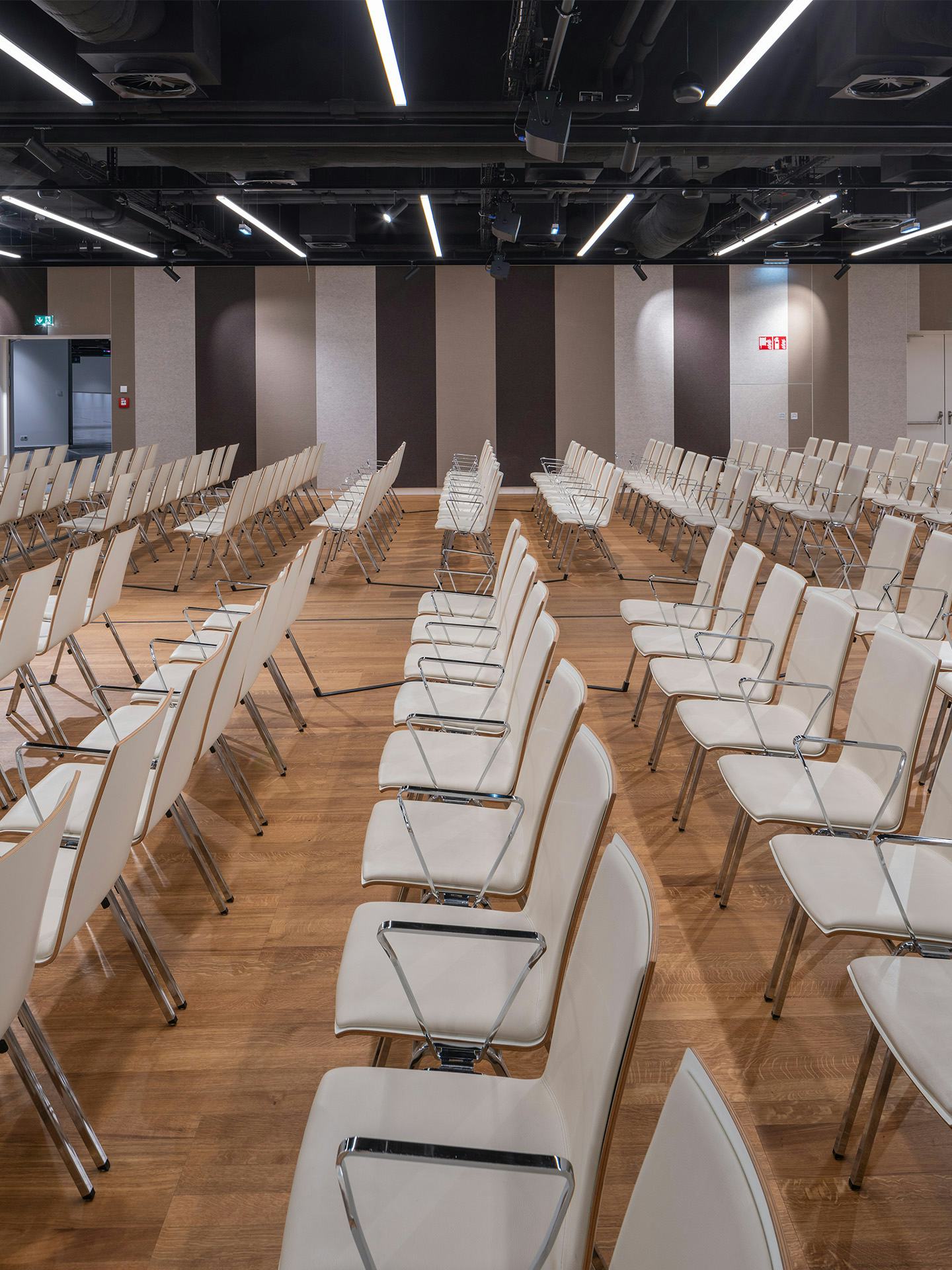 Foto: Sitzreihen in einem Saal mit Holzboden, gestreifte Tapete