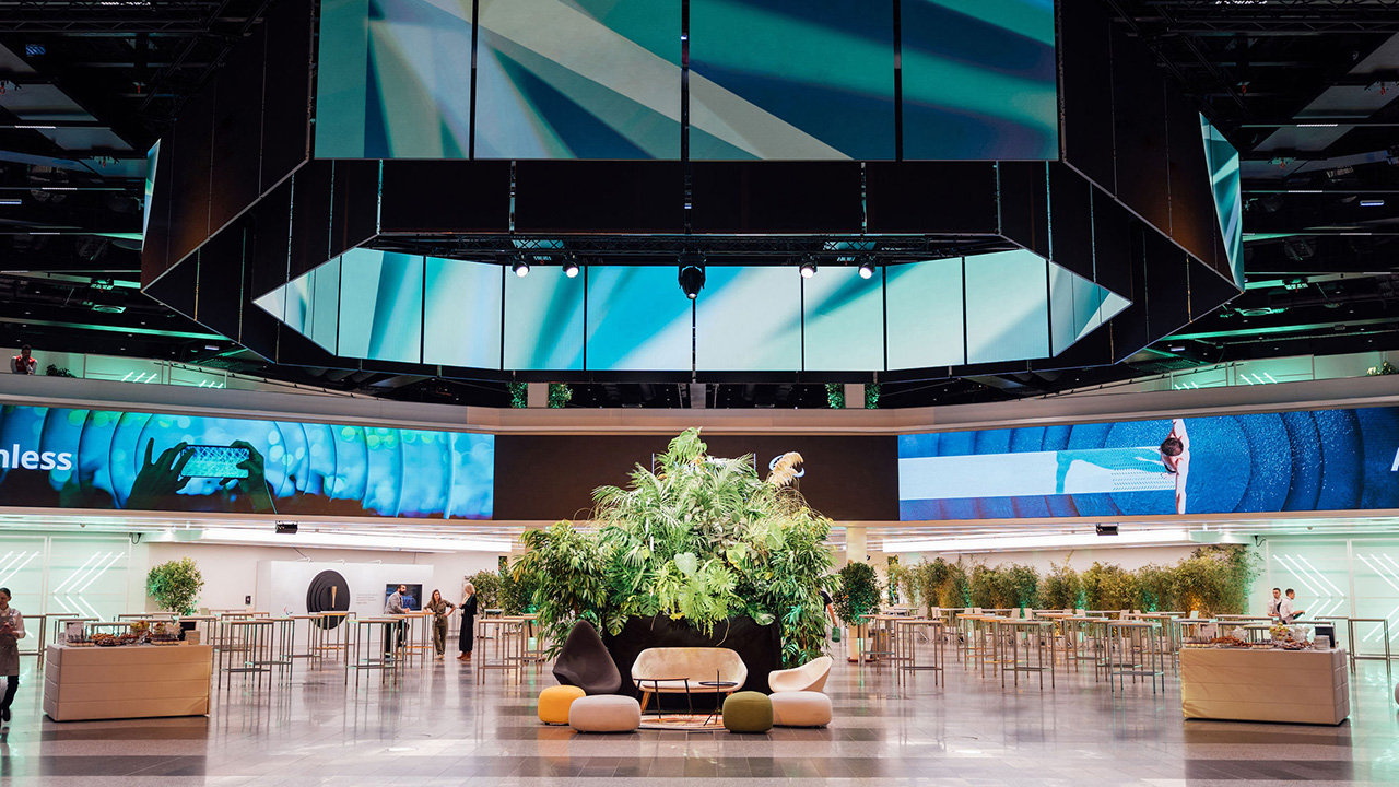 Foto: Halle mit blauen LED-Screens, Pflanzen und Tischen