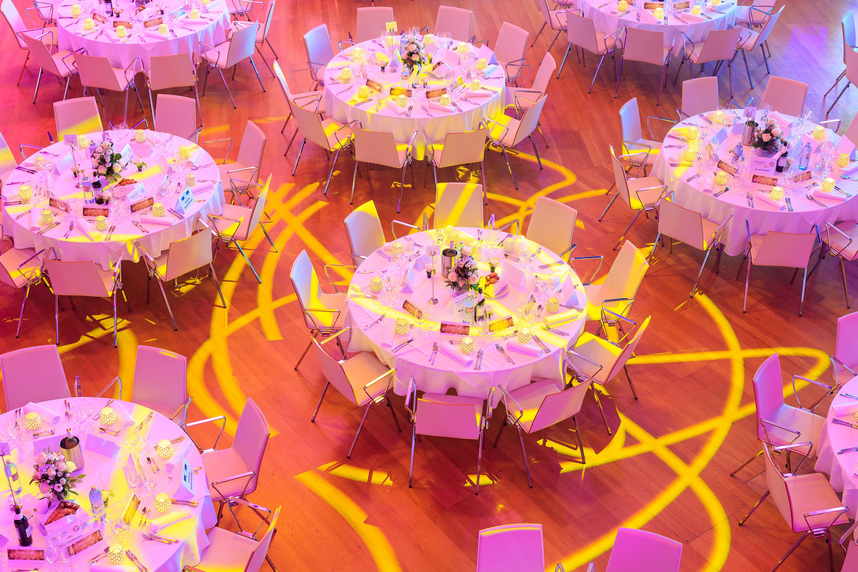Foto: Weiße Gala Tische auf Holzboden, gelbes Licht