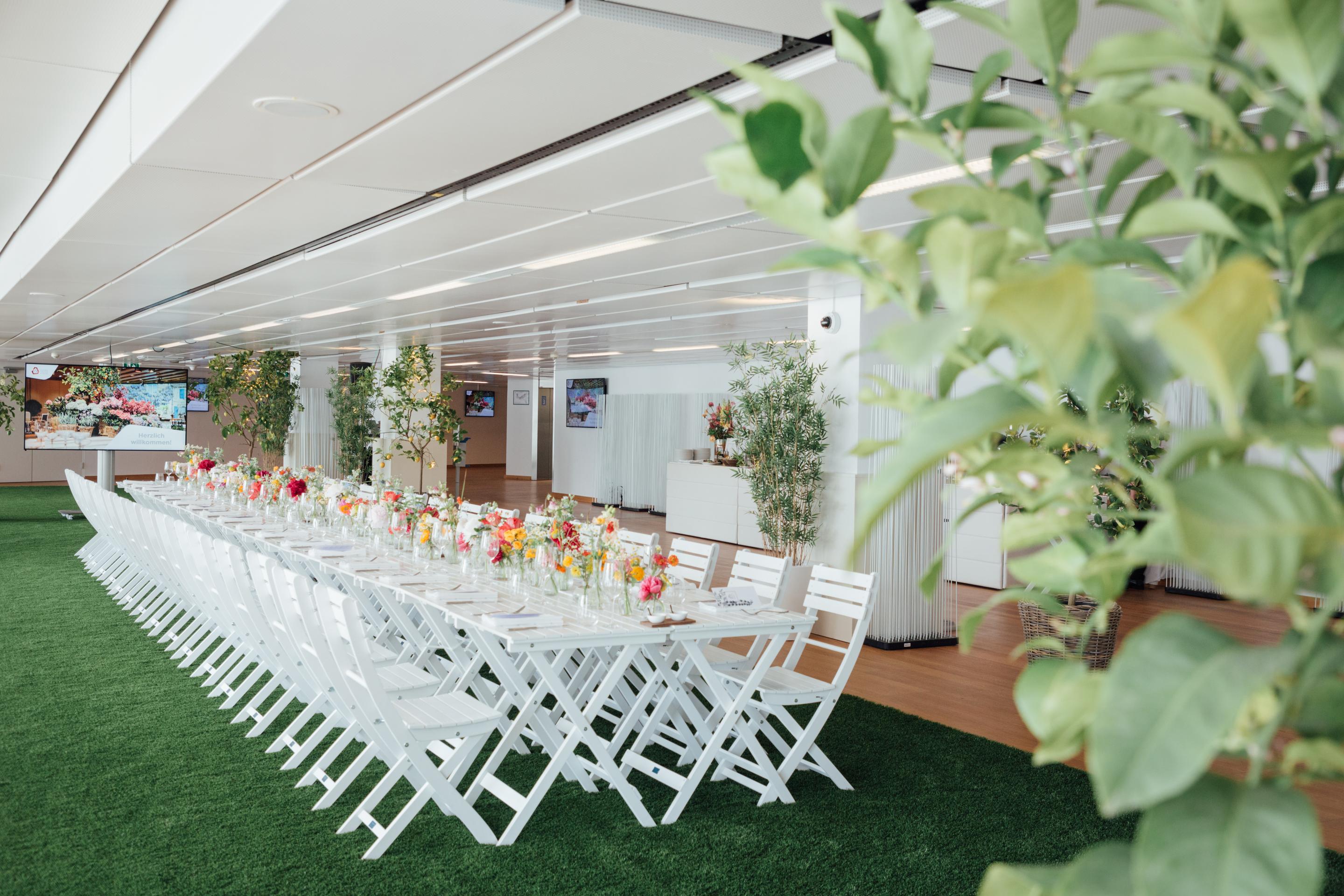 Foto: Weißer gedeckter Tisch in einem Raum mit grünem Teppich und Blumen