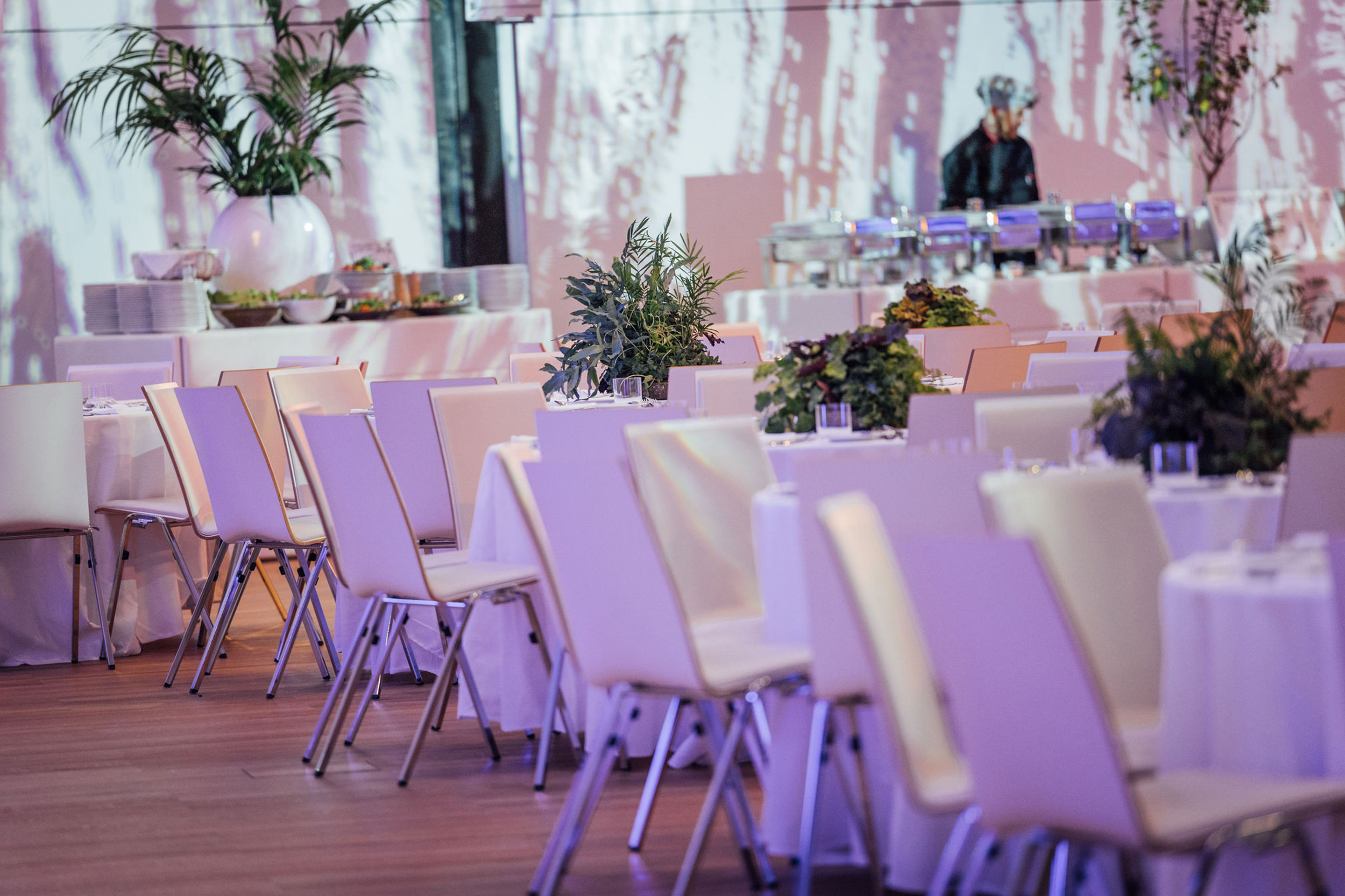 Foto: Gedeckte Tische mit Pflanzendeko, Catering, ein Mensch im Hintergrund