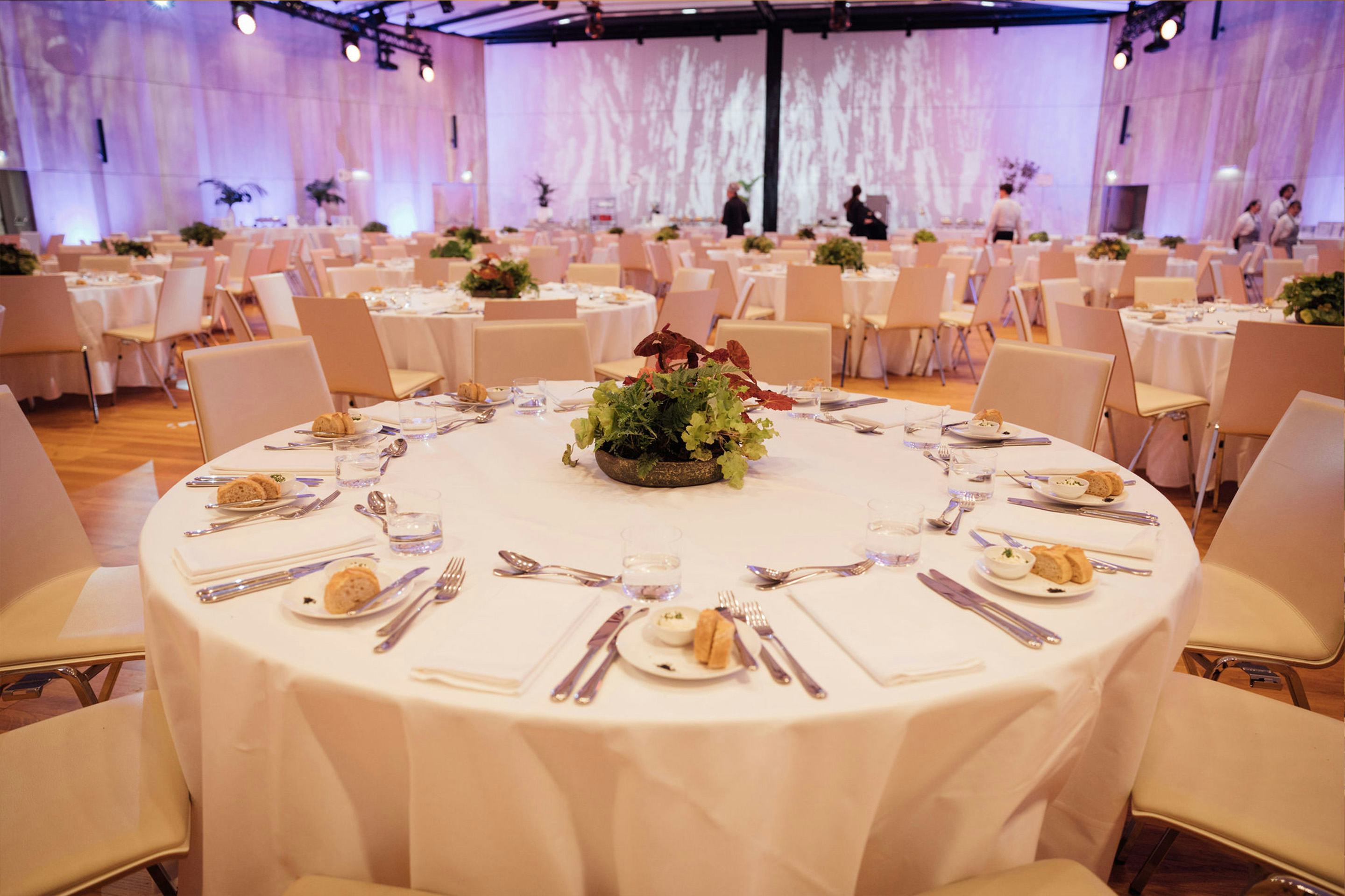 Foto: Runde gedeckte Gala-Tische mit Stuehlen in einem Raum mit Holzboden und einigen Menschen