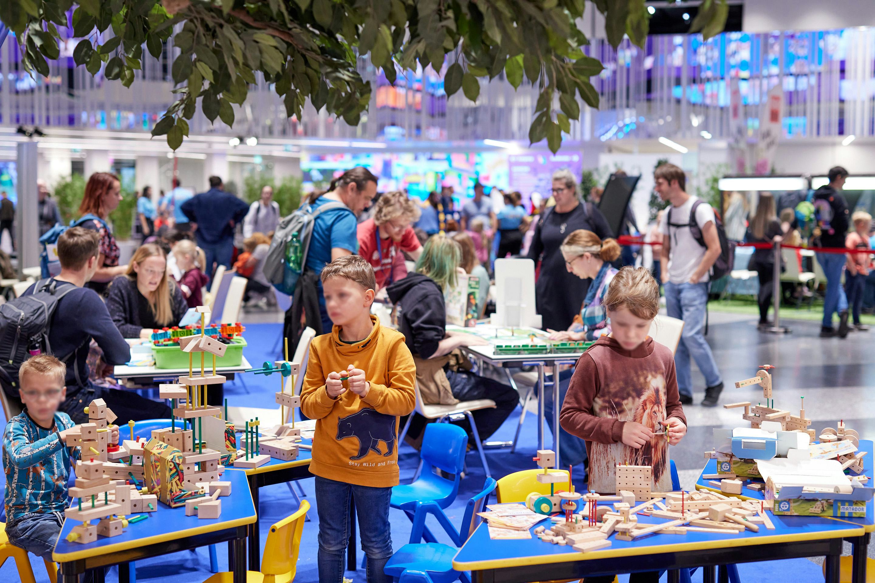 Foto: Kinder mit Bausteinen in einer Halle voller Menschen und Pflanzen