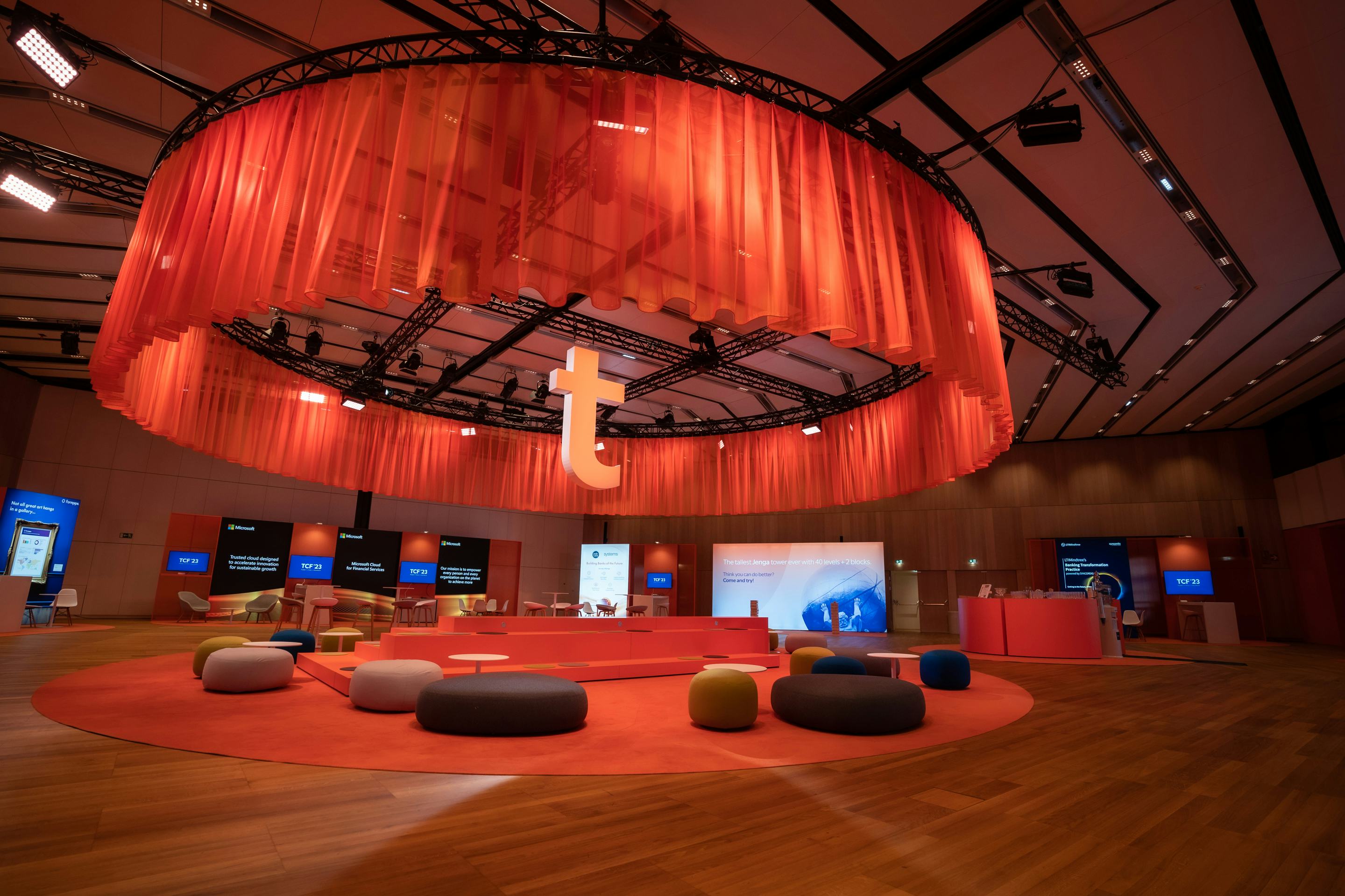 Foto: Raum mit rotem Decken-Vorhang, Networking-Bereichen und beleuchteten Screens