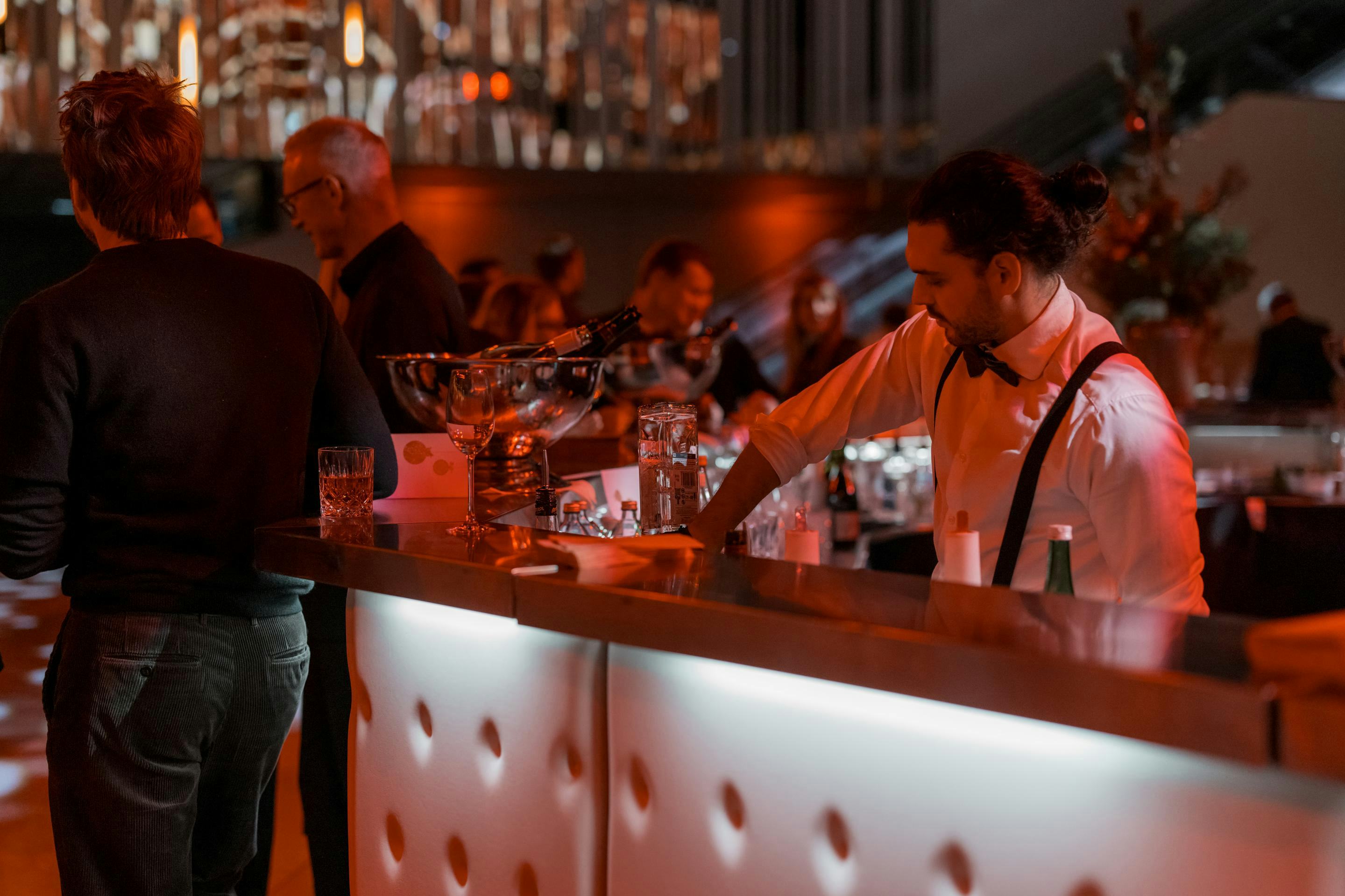 Foto: Barkeeper mixt Getraenk an einer Bar mit Menschen im roten Licht