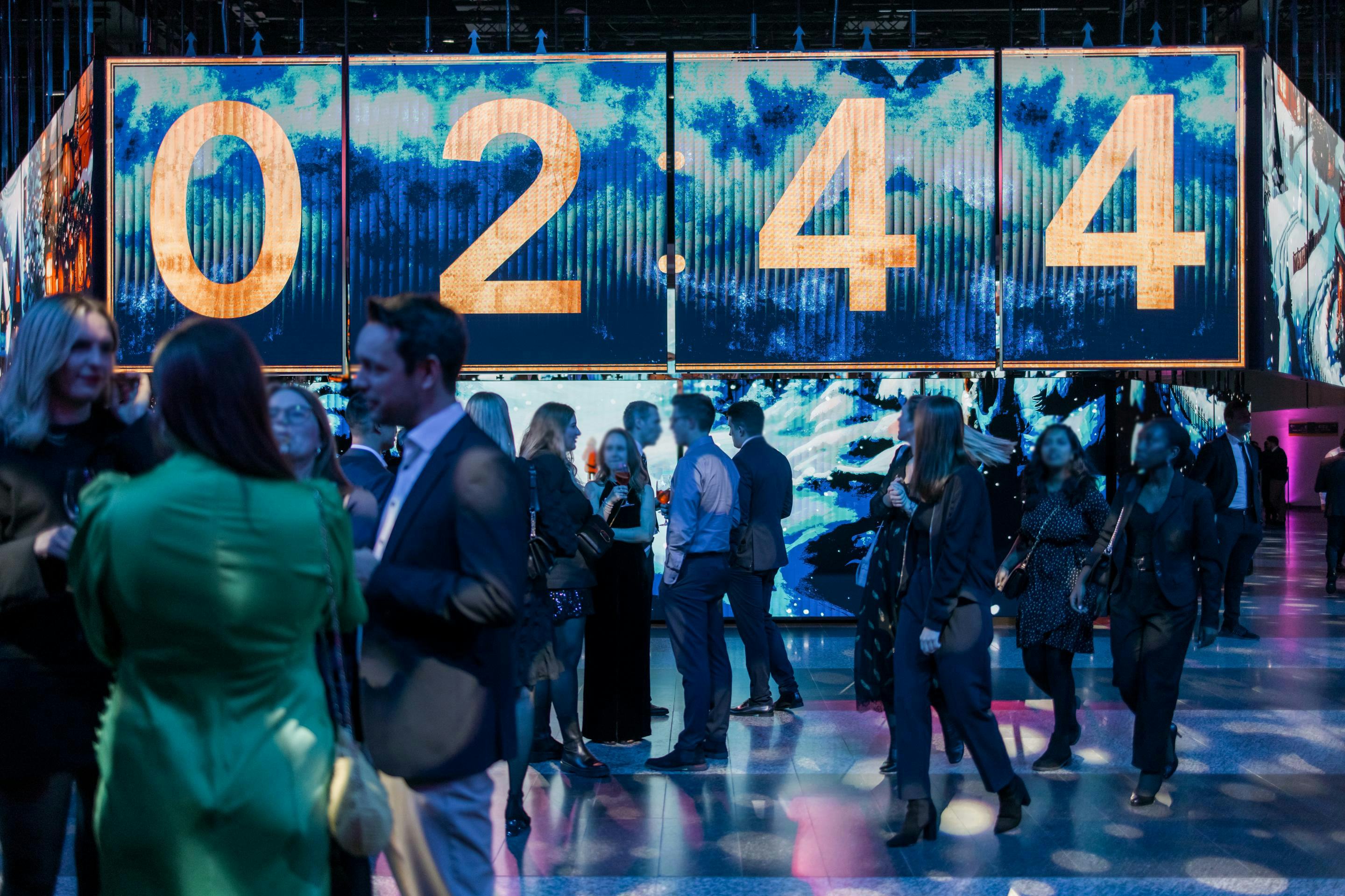 Foto: Countdown auf LED-Flaechen in einer Halle mit festlich gekleideten Menschen