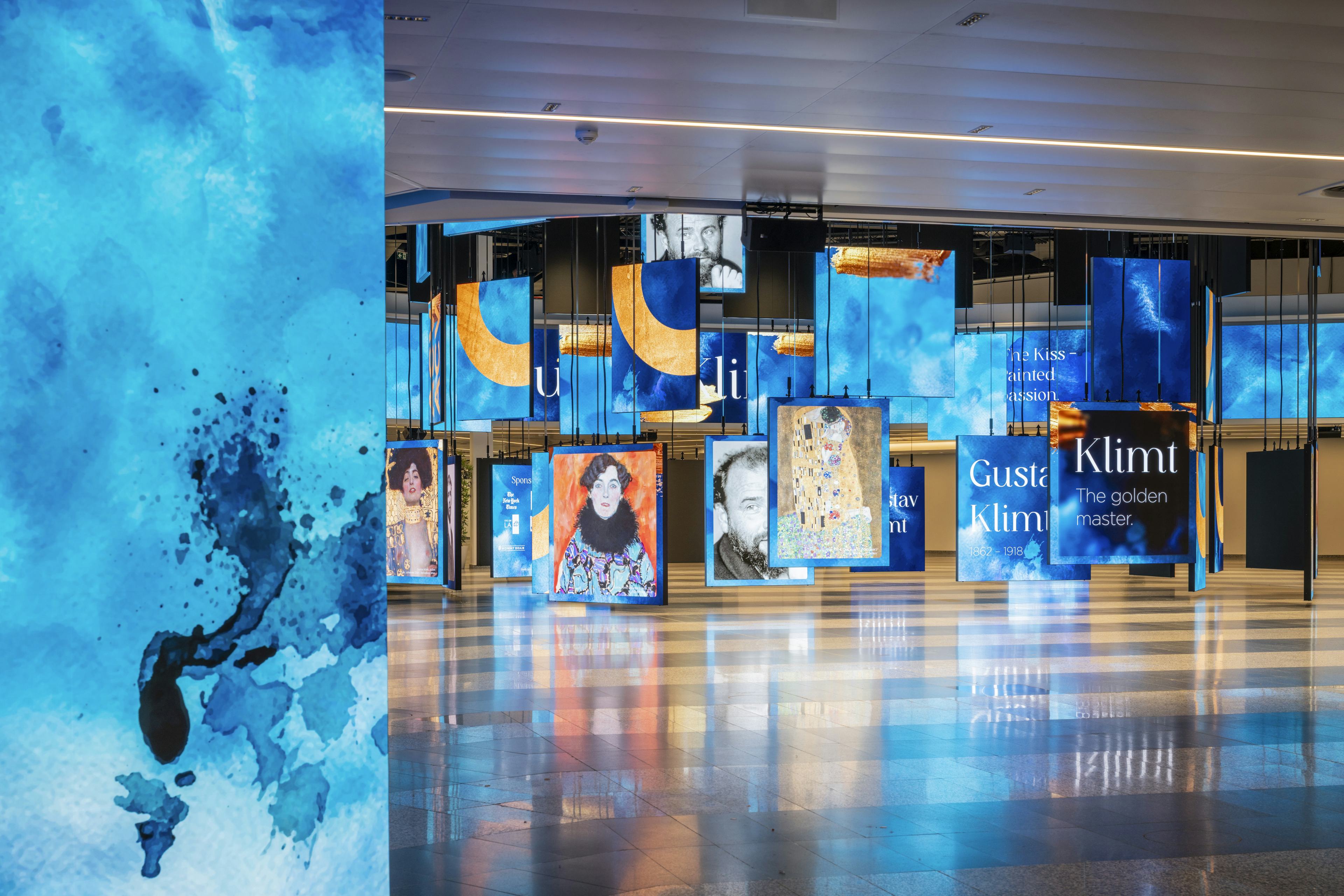 Die Eingangshalle des Austria Center Vienna mit beleuchteter polySTAGE LED-Installation, die Fotos von Klimt Kunstwerken zeigt.