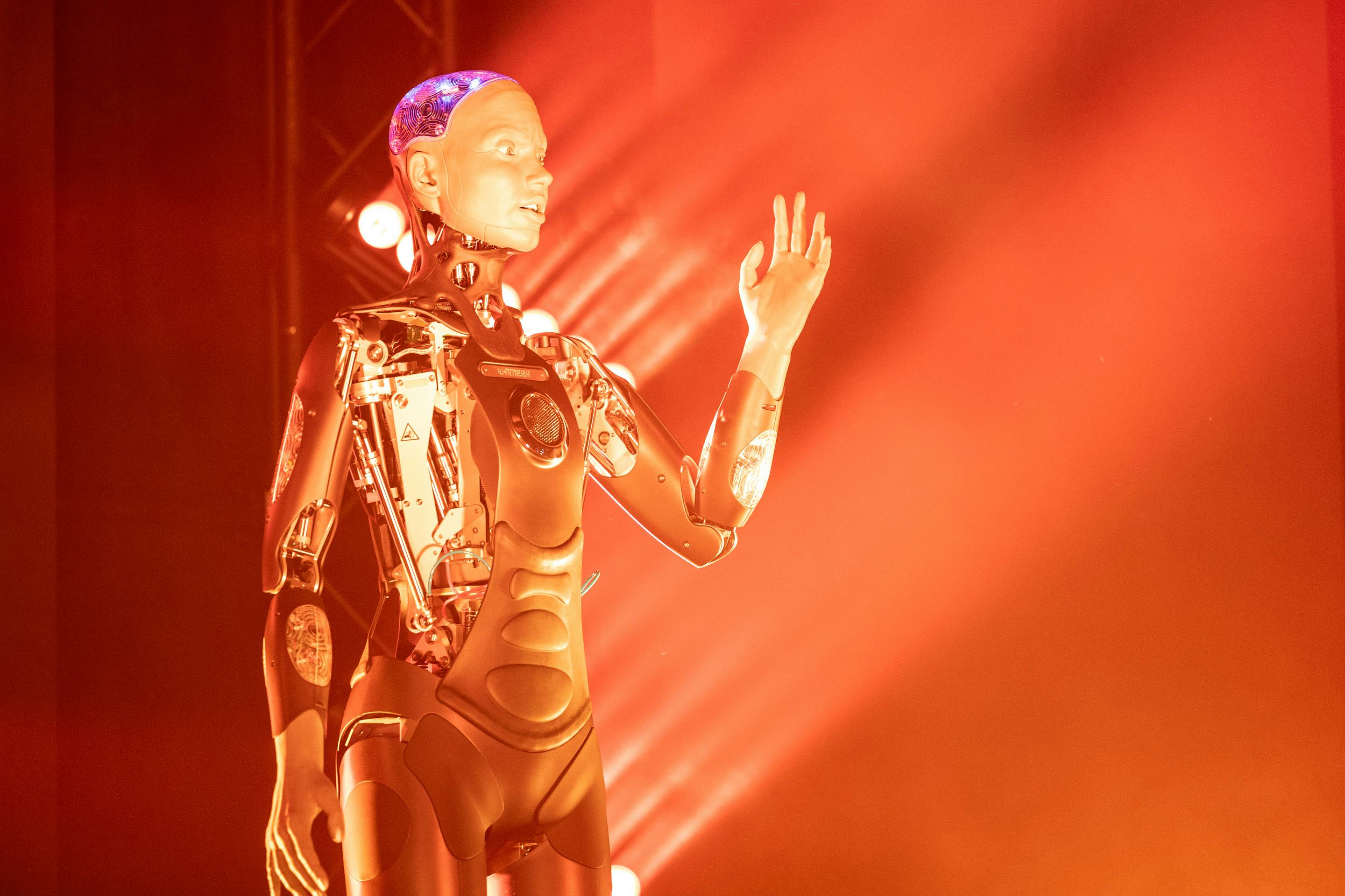 Foto: Roboter, der einen Arm ausstreckt. Im Hintergrund orange Beleuchtung