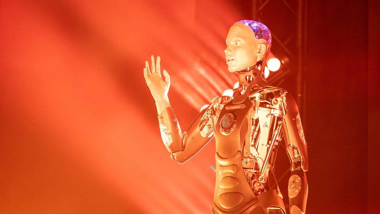 Foto: Roboter, der einen Arm ausstreckt. Im Hintergrund orange Beleuchtung