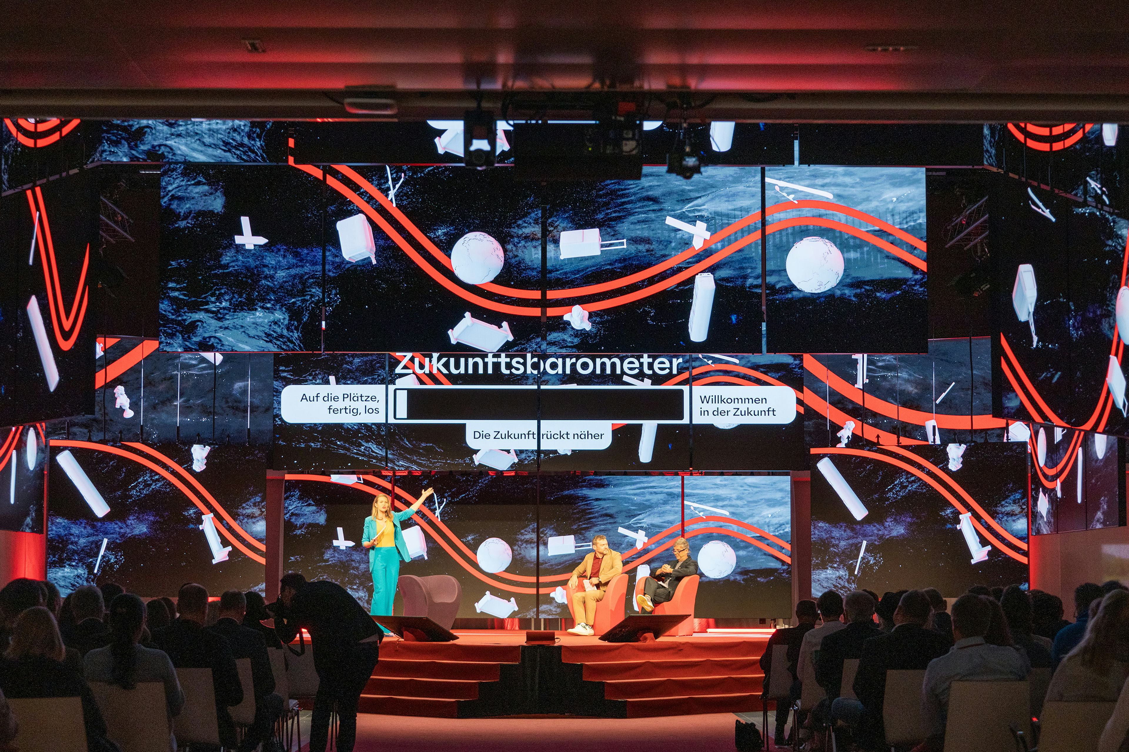 Eine Moderatorin und einige Speaker auf der polySTAGE Buehne vor Publikum im Austria Center Vienna.