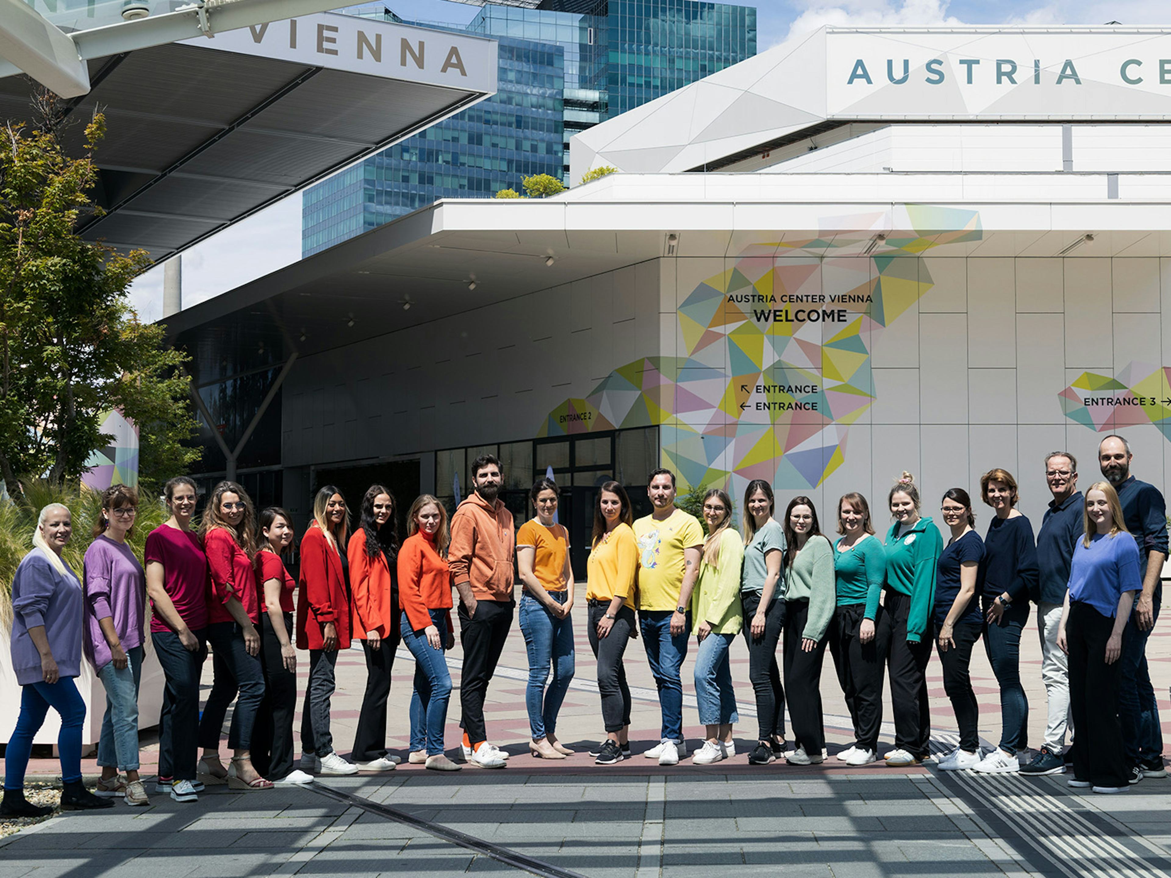 Mitarbeiterinnen des Austria Center Vienna stehen in einer Reihe aufgestellt in den Farben des Regenbogens.