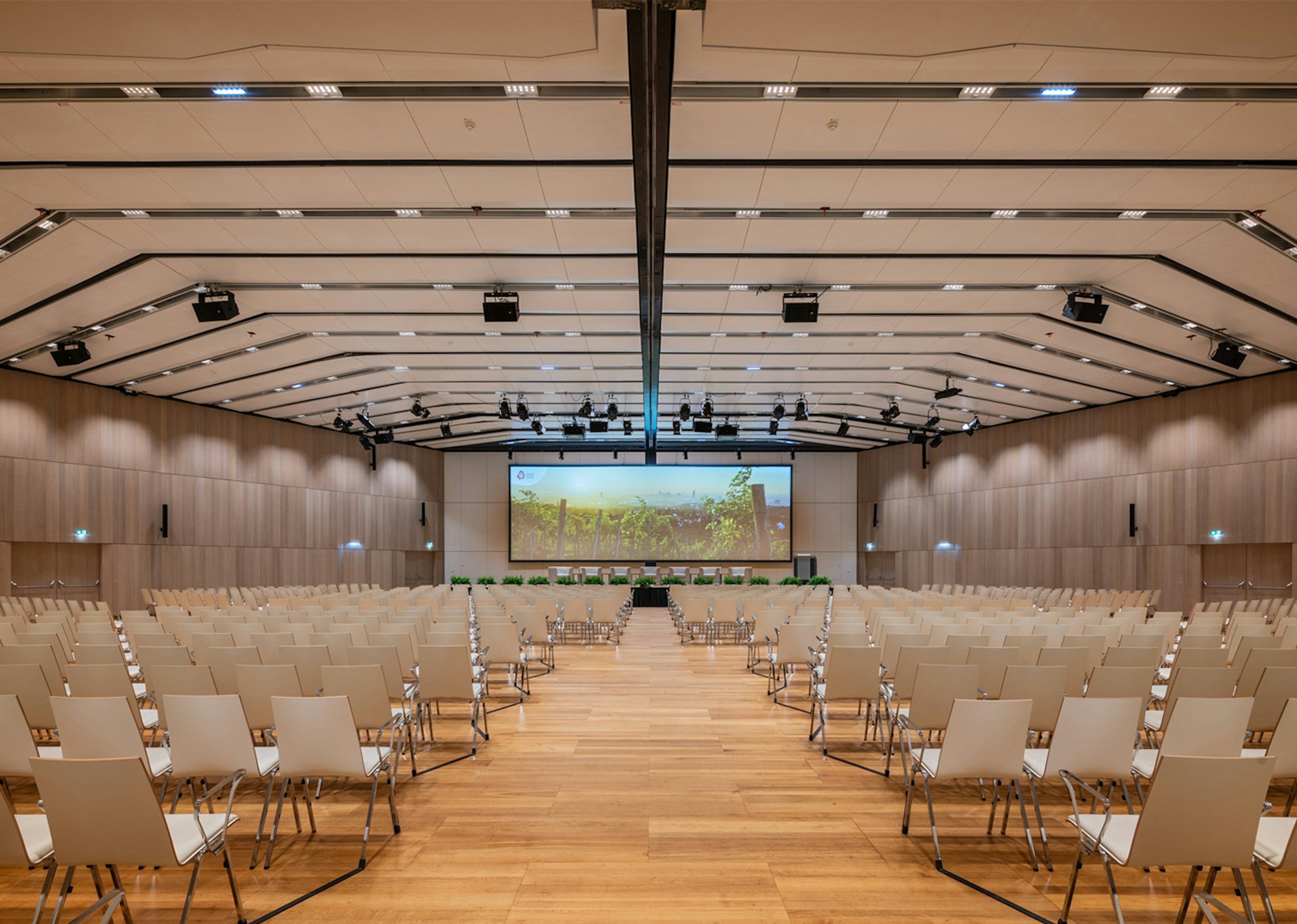 Holzverkleideter Saal F im Austria Center Vienna mit Sitzreihen und einer Leinwand.